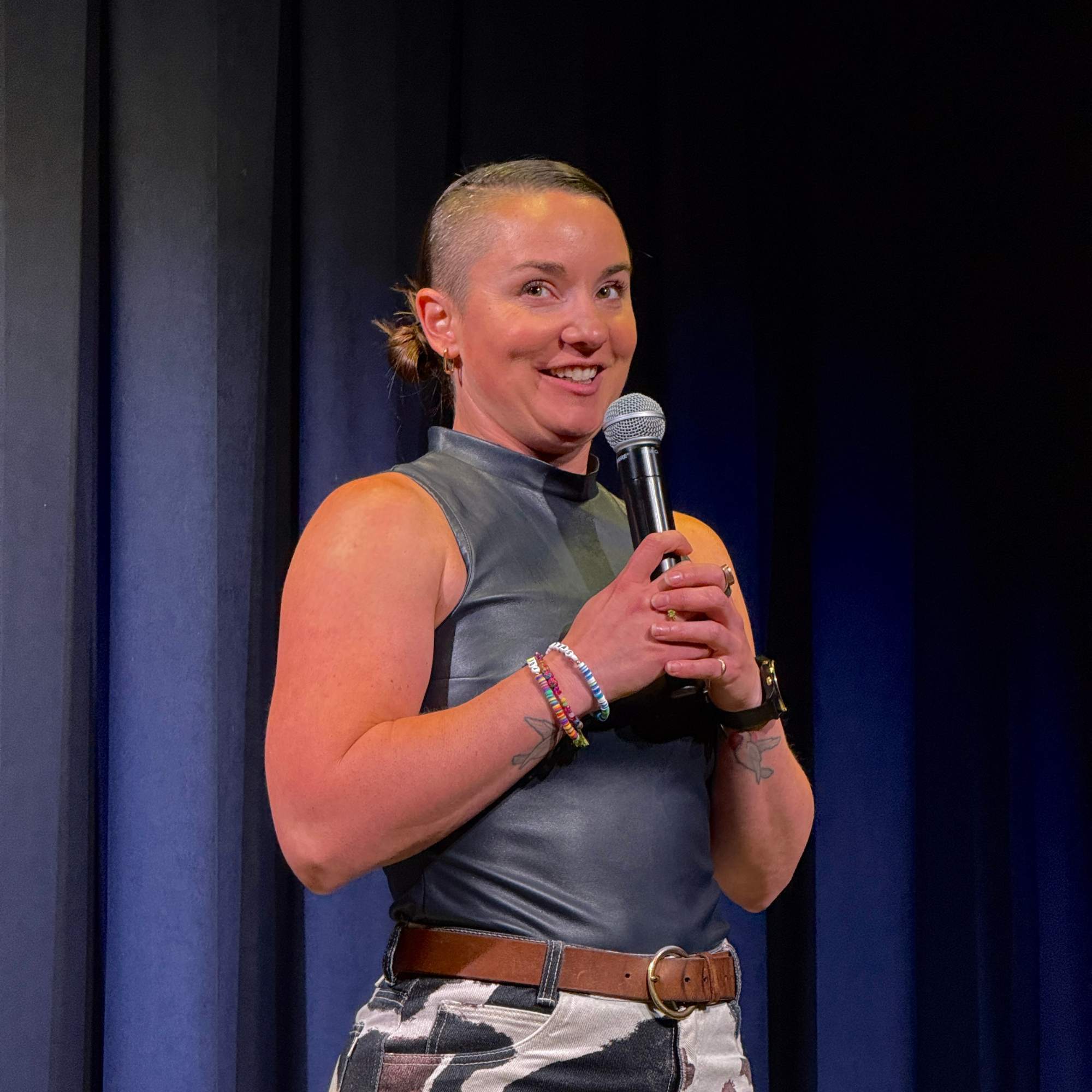 Comedian smiling mid-set in front of the blue curtain at the Snowmass Live Comedy Series, The Collective Snowmass