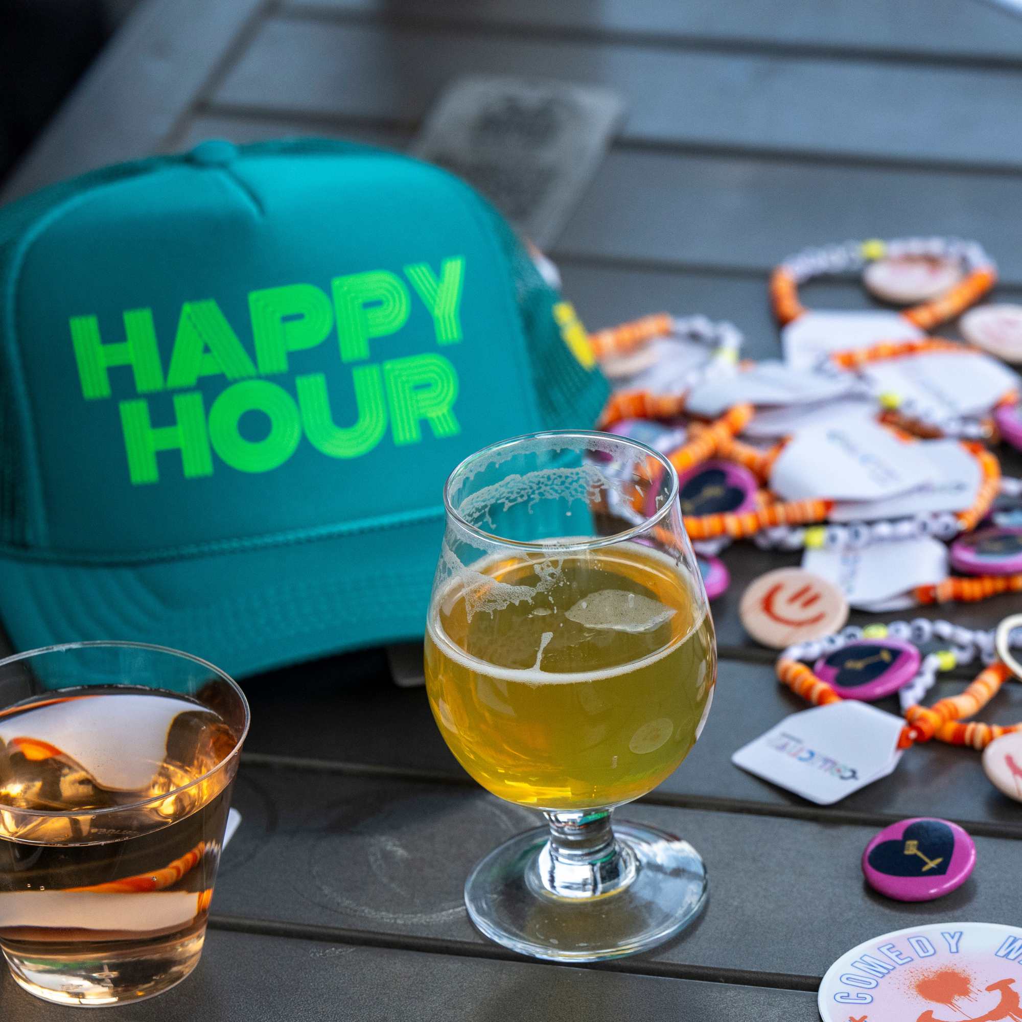 Happy Hour hat, drinks and festival buttons on a patio table at Snowmass Live Comedy WKND!, The Collective Snowmass