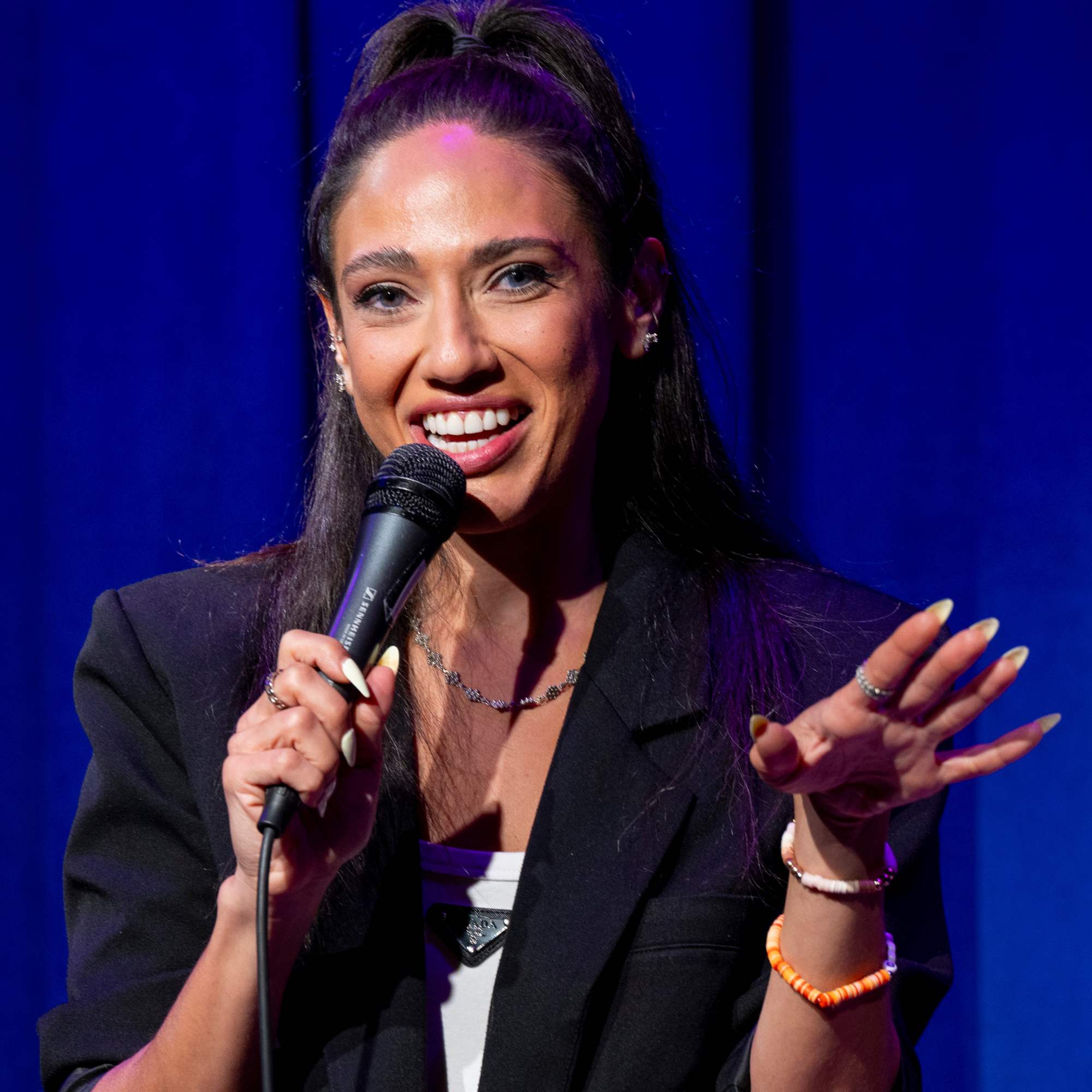 Comedian smiling mid-joke under blue stage lights at Snowmass Live Comedy WKND!, The Collective Snowmass