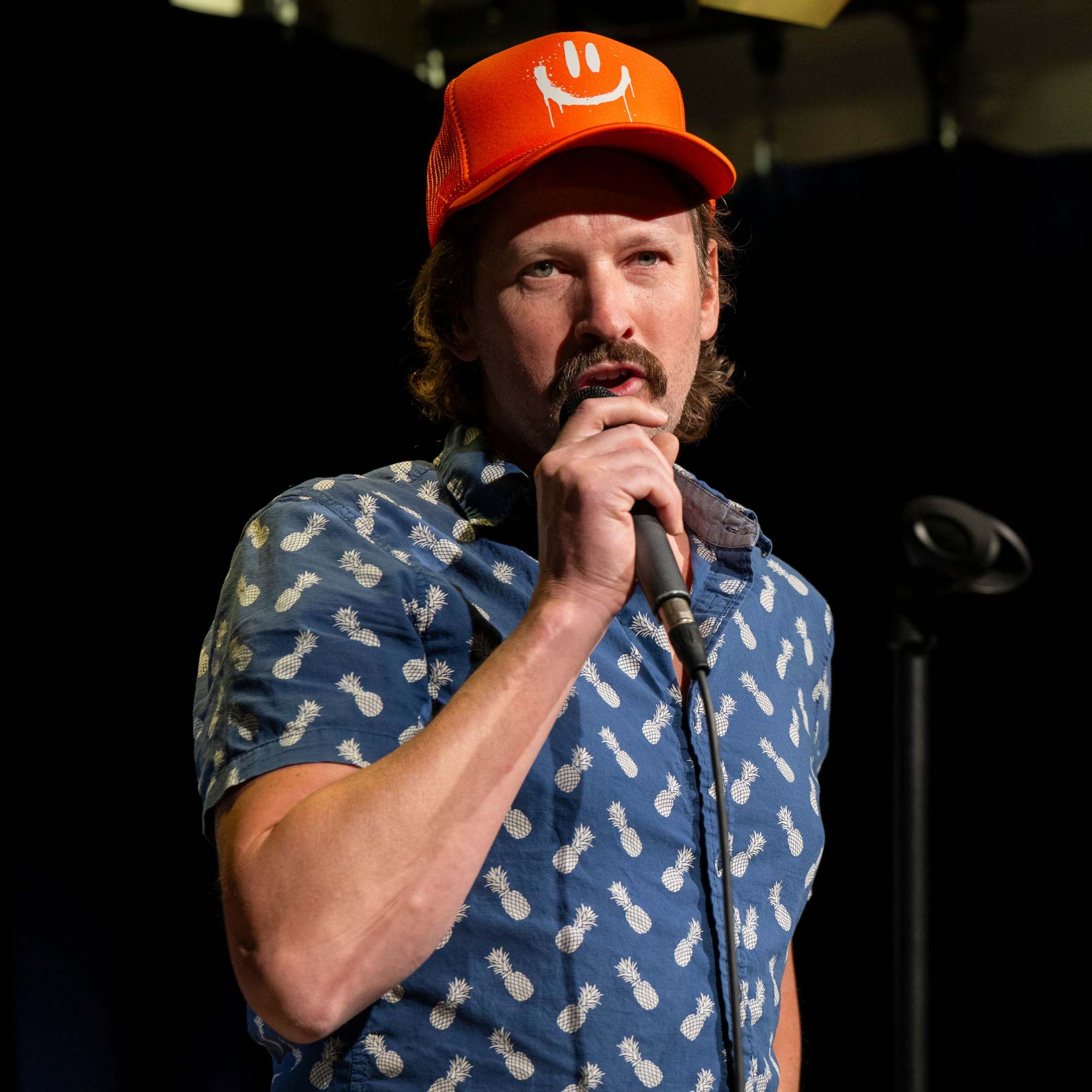 Comedian in an orange smiley-face hat performing at Snowmass Live Comedy WKND!, The Collective Snowmass