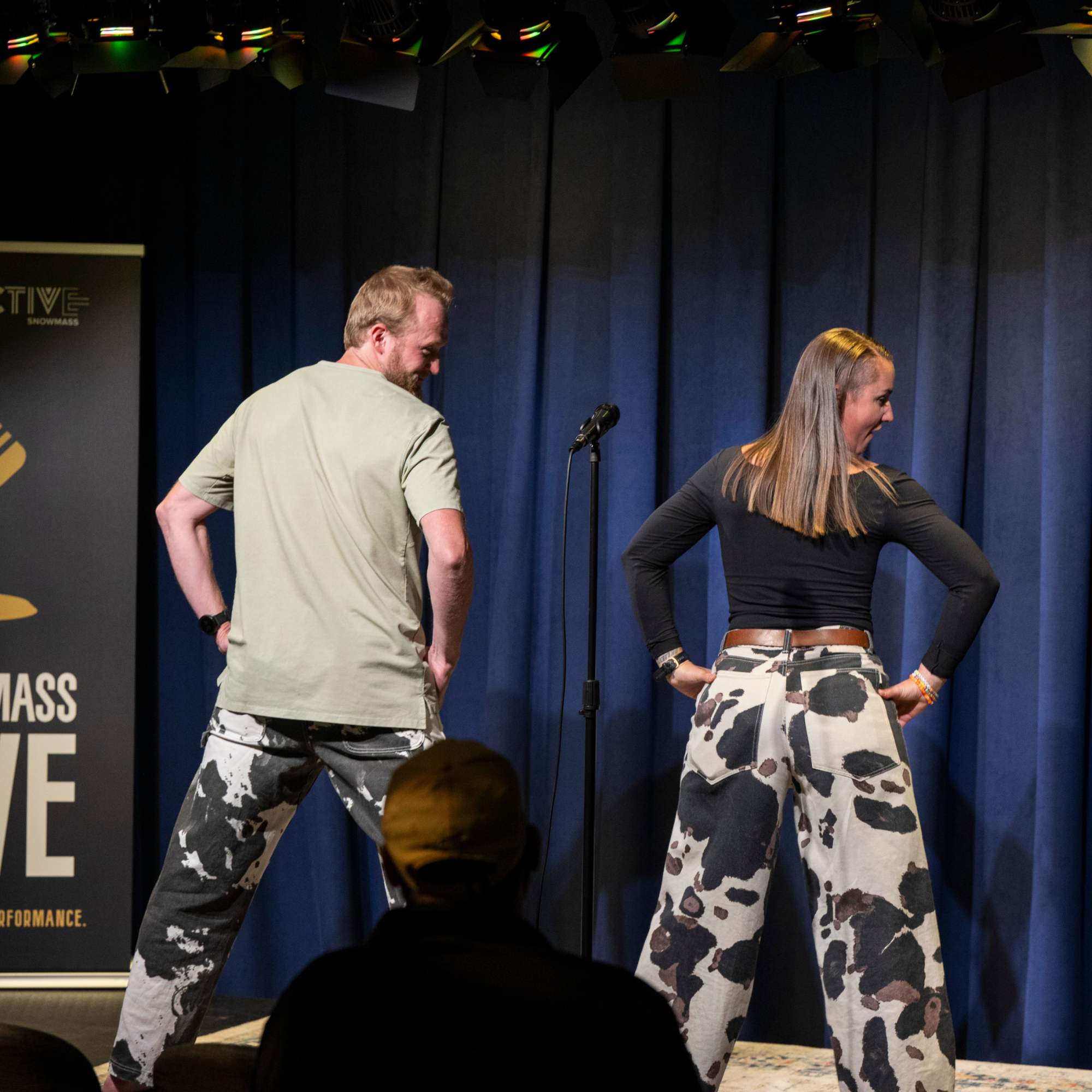 Two comedians in cow-print pants facing the backdrop on stage at Snowmass Live Comedy WKND!, The Collective Snowmass