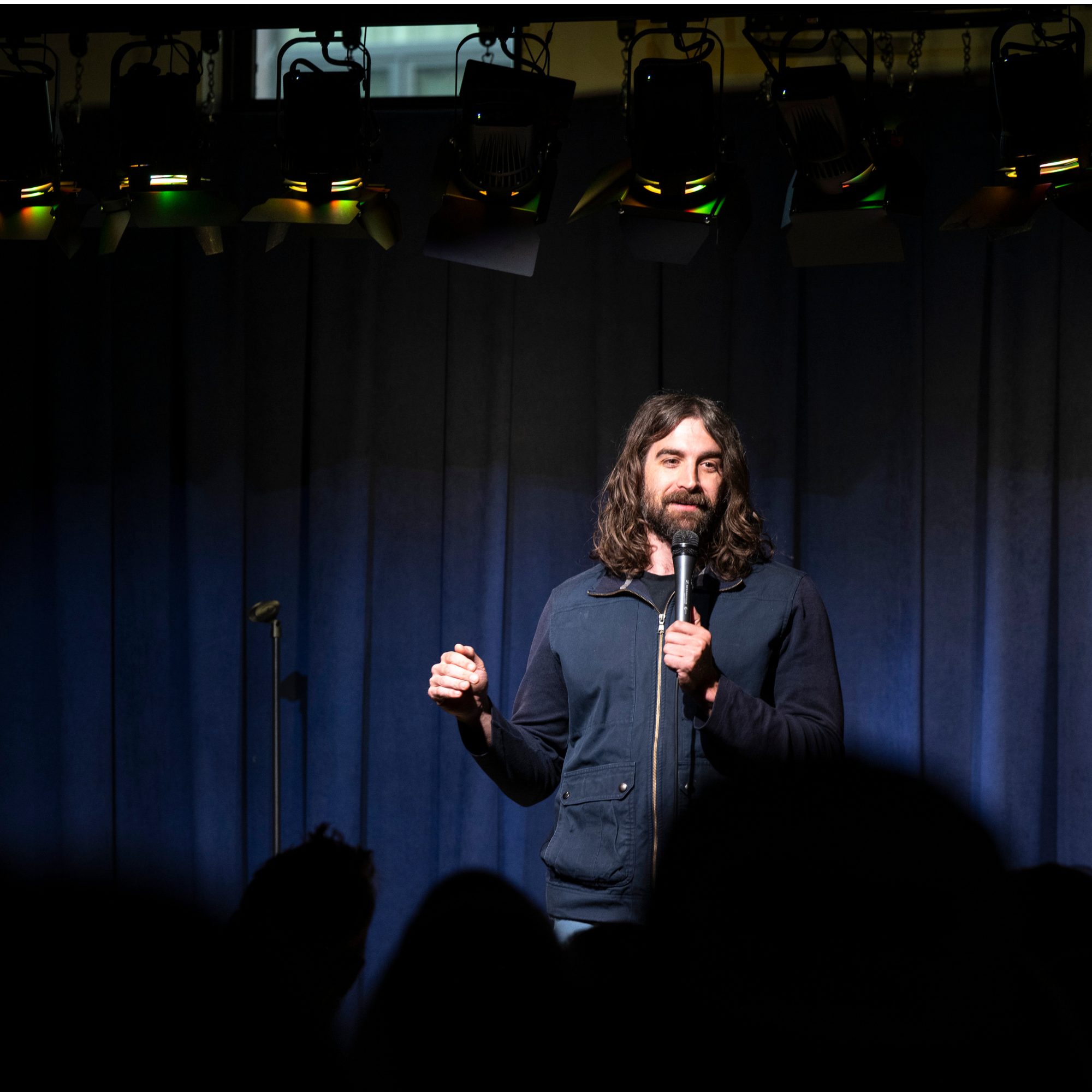 Comedian performing on a dark stage under spotlights at Snowmass Live Comedy WKND!, The Collective Snowmass